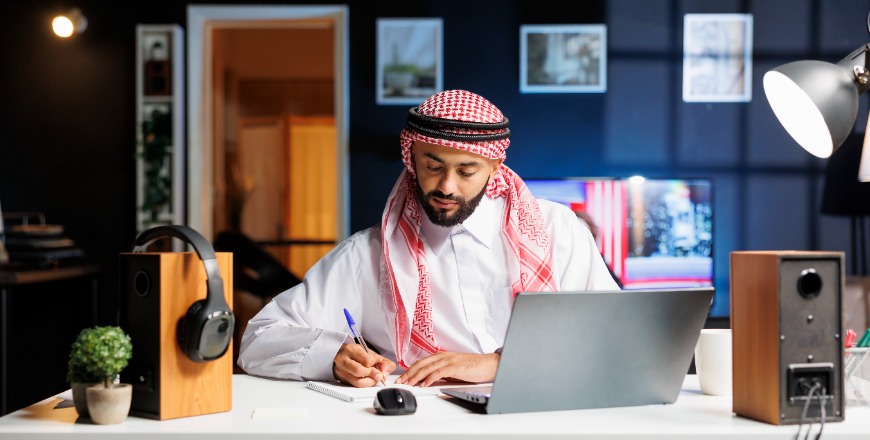 arab-man-works-efficiently-browsing-internet-takes-notes-communicates-digitally-his-modern-office-young-muslim-guy-doing-research-writing-his-notebook-870x440